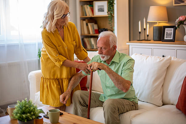 istock Senior man getting up from sofa with walking stick and wife helping him 2228542676