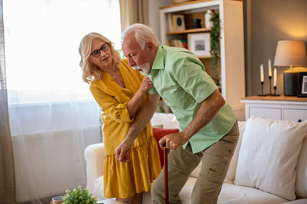 Senior man getting up from sofa with wife helping him at home