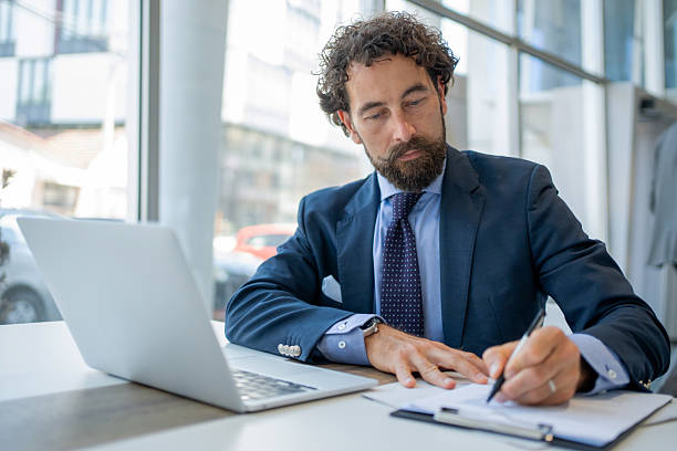 istock Focused businessman working on laptop and taking notes in modern office 2228544284