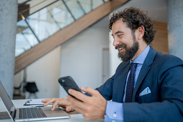 istock Smiling businessman using laptop and smartphone in modern office 2228544439
