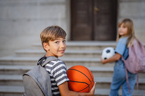 Elementary school students are leaving school after class, carrying backpacks and balls, ready for extracurricular activities or to go home and play