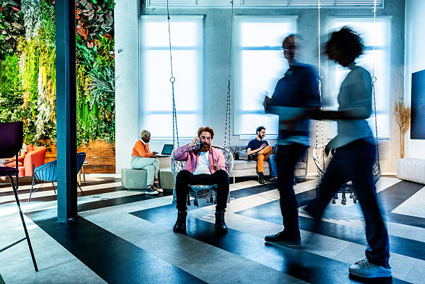 Multiethnic startup business team on meeting in a modern bright open space coworking office. Brainstorming, working on laptop. Group of coworkers walking around in motion blur.