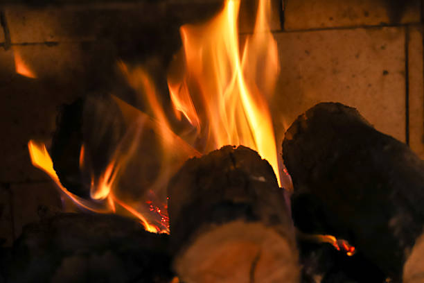 A scene of a fireplace. A dramatic close-up reveals the intense heat and vibrant colors of the burning coals. Orange, red, and blue flames dance around the embers.