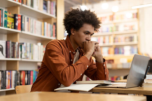 istock Serious and focused African American student guy sitting in library, preparing for lecture or exam. Knowledge and learning concept 2228554992