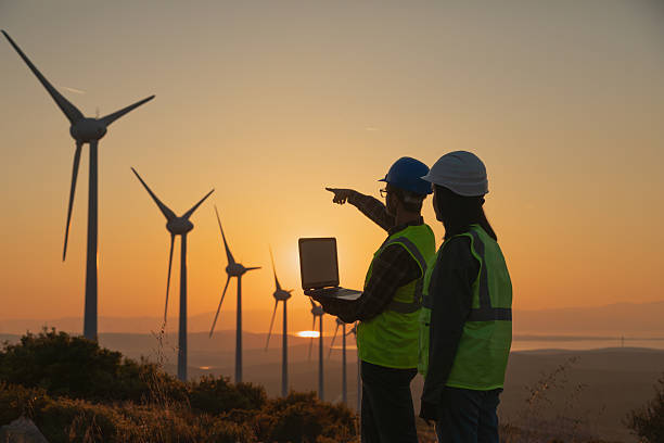 istock Engineers with Safety Helmets and Laptop Analyzing Wind Turbines at Sunset, Emphasizing Renewable Energy, Sustainability, and Green Technology Innovation 2228556383