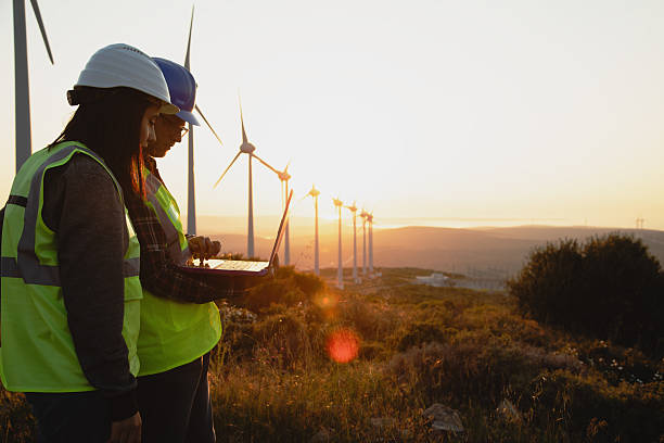 istock Engineers with Safety Helmets and Vests Using Laptop at Wind Farm During Sunset, Highlighting Renewable Energy, Sustainability, and Green Technology Innovation 2228556388