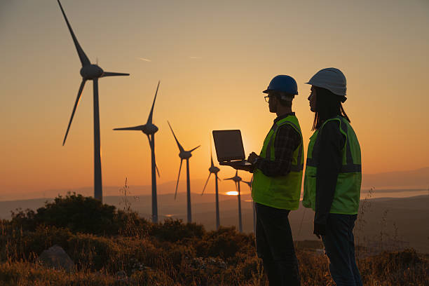 istock Engineers with Safety Helmets and Vests Using Laptop at Wind Farm During Sunset, Highlighting Renewable Energy, Sustainability, and Green Technology Innovation 2228556398