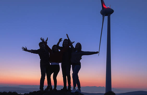 istock Group of Friends Posing with Open Arms at Wind Farm During Blue Hour, Emphasizing Friendship, Joy, and Sustainability 2228557140