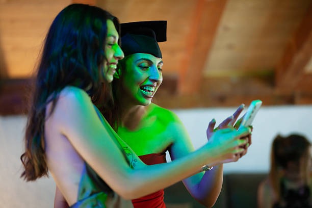 Two happy women celebrating a graduation while looking at a smartphone together