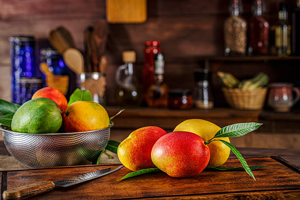 Group of mangos on a cutting board in a rustic kitchen. Natural window lighting.