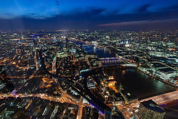 View of London at night fall features illuminated landmarks like the London Eye, Hungerford Bridge, and the Houses of Parliament, all bathed in a warm, sepia-toned glow along the River Thames.
