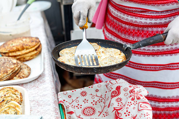 A person is cooking pancakes on a pan. There are several pancakes on a table in front of the person