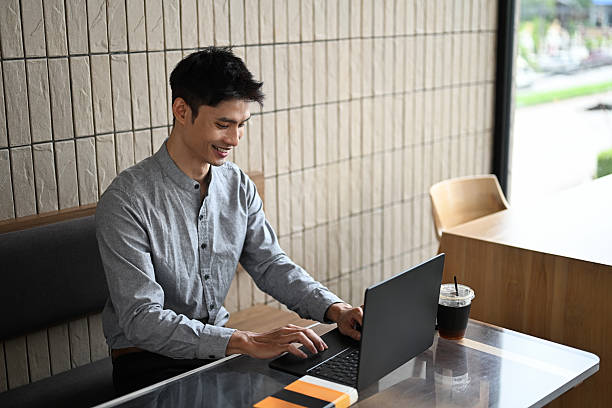 istock Businessman typing on laptop while sitting at a wooden table with iced coffee 2228590313