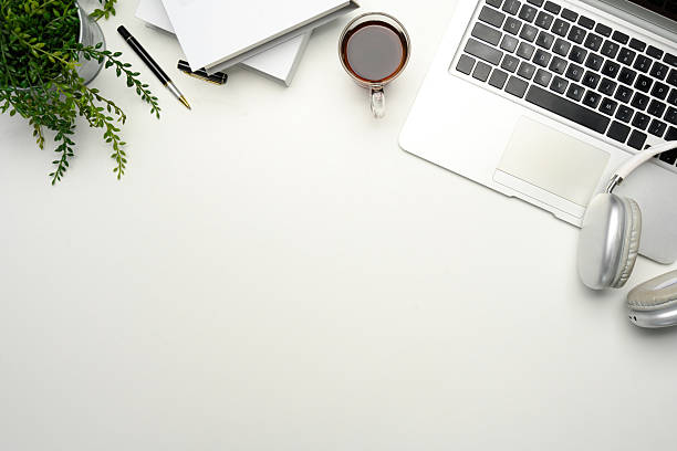 Minimalist workspace with laptop, coffee cup, headphones and notebooks on white desk