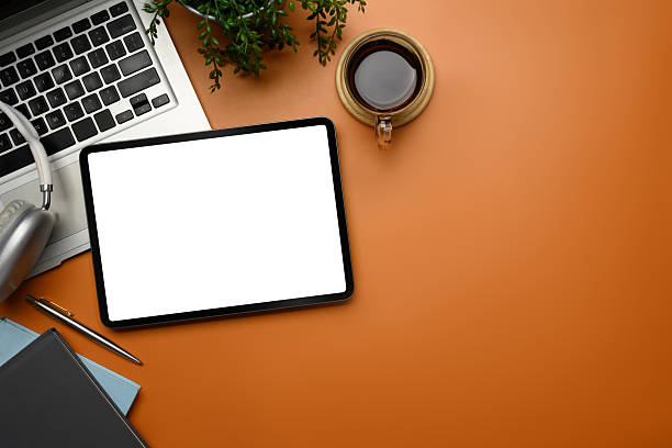 istock Creative office desk with digital tablet, laptop, coffee, and headphone on orange background 2228590511