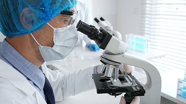 istock Senior male scientist wearing a protective mask, cap, and gloves, examining samples under a microscope in a modern laboratory. Medicine, healthcare and science concept 2228595402