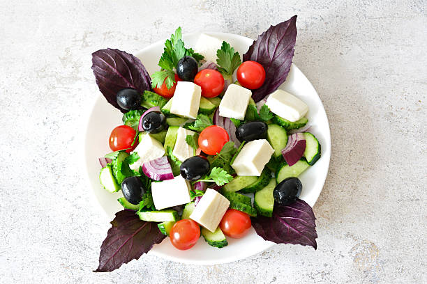Fresh and vibrant Greek salad with feta cheese, olives, basil and tomatoes top view