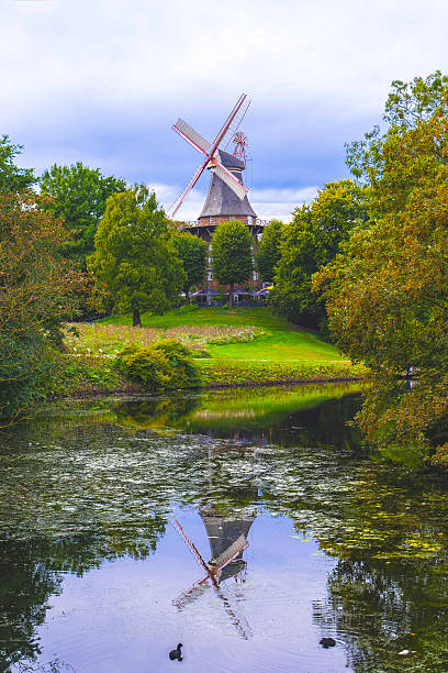 istock Scenic windmill reflected in calm pond surrounded by lush greenery on a peaceful summer day 2228596303