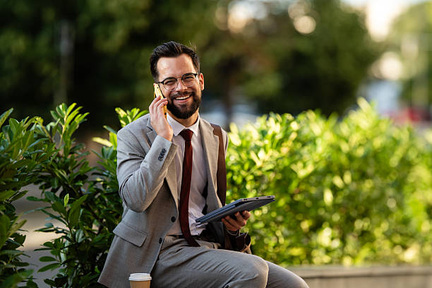 istock Businessman talking on phone and holding tablet while smiling outdoors 2228596391