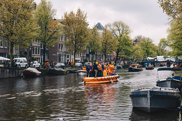 Amsterdam, Netherlands - 27 Apr, 2024 - Festive street scenes during King's Day in Amsterdam, with crowds dressed in orange enjoying music, boats, markets, and urban festivities across the city center.