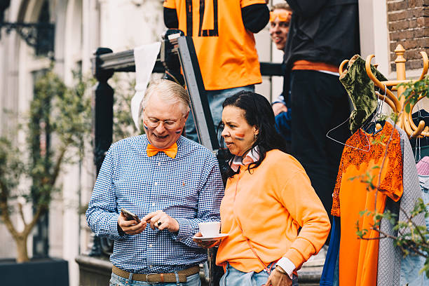 Amsterdam, Netherlands - 27 Apr, 2024 - Festive street scenes during King's Day in Amsterdam, with crowds dressed in orange enjoying music, boats, markets, and urban festivities across the city center.