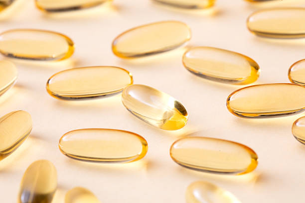 A cluster of golden softgel vitamin capsules placed on a neutral beige background.