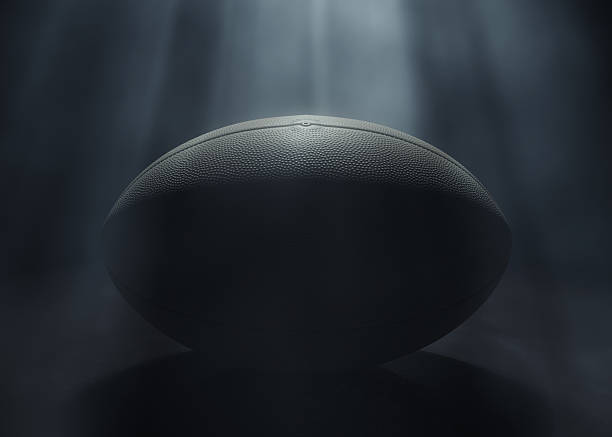 A generic rugby sports ball being lit by a single ethereal light rays on a dark black background - 3D render
