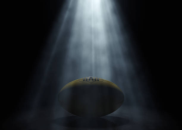 An aussie rules sports ball being lit by a single ethereal light rays on a dark black background - 3D render