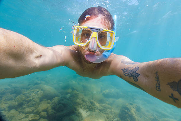 Young man with tattoos taking a selfie while snorkeling underwater in a tropical sea