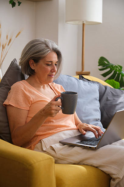 istock Mature woman relaxing on sofa using laptop and drinking coffee 2228609886