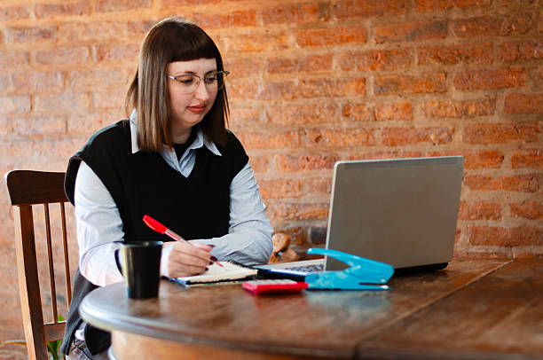istock Smile young female employee or student wearing glasses working study from home office with a laptop and taking notes 2228611389