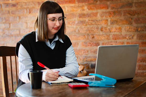 istock Smile young female employee or student wearing glasses working study from home office with a laptop and taking notes 2228611392
