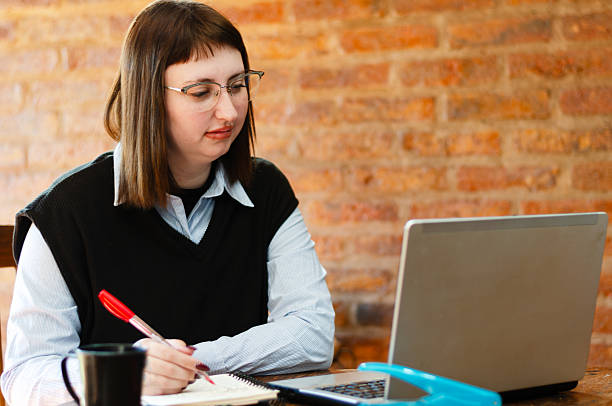 istock Smile young female employee or student wearing glasses working study from home office with a laptop and taking notes 2228611410