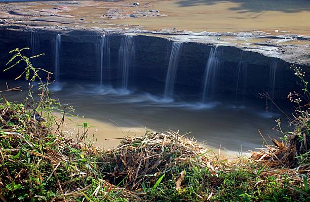 The silky water falls in parallel streams, framed by wild vegetation in the foreground. long exposure of Ciliwung River