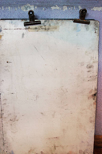 istock Old worn drawing board with two rusty metal binder clips, mounted against a faded pastel textured wall. 2228617883