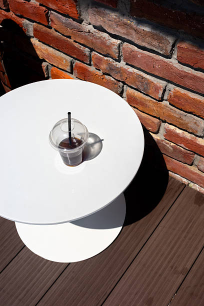 A refreshing iced coffee sits on a white table with a rustic brick wall background. The composition highlights the contrast and detail.