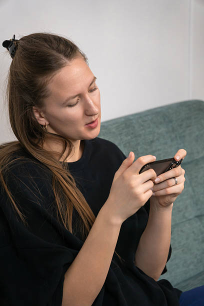 istock Homely dressed young woman sitting on a comfortable sofa, enjoying a mobile game at home, fully immersed in the digital world of entertainment and leisure. Vertical photo 2228630489