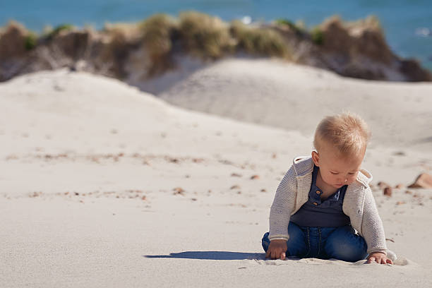 istock Cute Baby Sitting in Sand – Ocean Background 2228630635