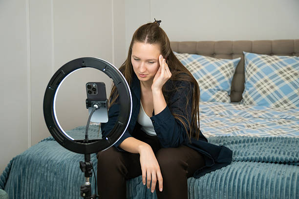 istock Young woman engaging in content creation using a smartphone and ring light setup in a cozy bedroom. Casual and relaxed atmosphere with a focus on digital media and online communication 2228630654