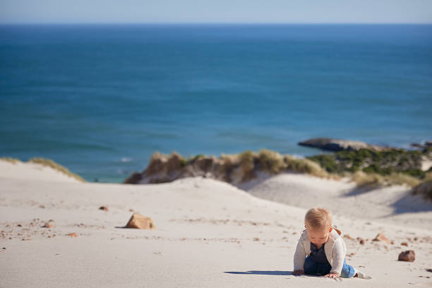 istock Cute Baby Sitting in Sand – Ocean Background 2228630688