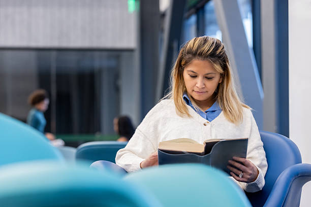 istock Mature woman reads a book while sitting in modern library 2228633913