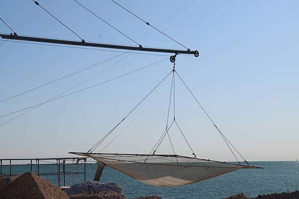 Fishing net hanging from a crane over the calm sea, ready for fishing activities