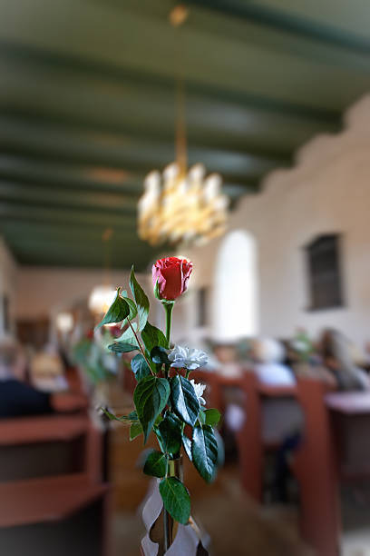 An artistic arrangement featuring a rose (Rosa spp.) adorned with delicate floral accents, placed as part of a ceremonial display within a peaceful chapel. Soft light enhances the serene atmosphere.