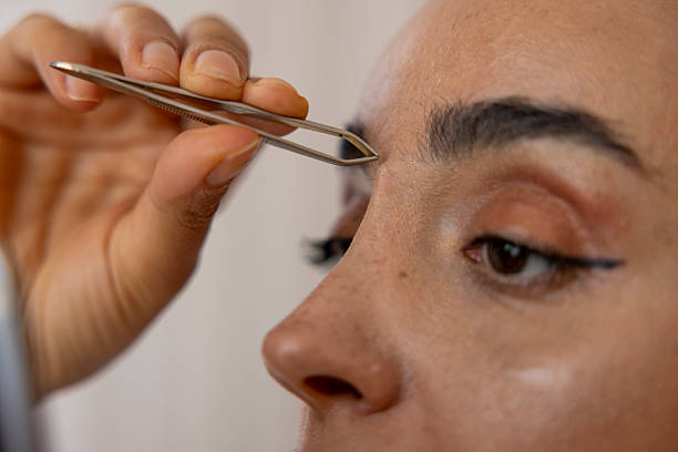 Woman shaping her eyebrows with tweezers