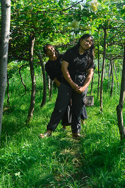 The teens beam with energy as they stand close together, smiling brightly while posing in a vineyard ridge surrounded by green leaves.