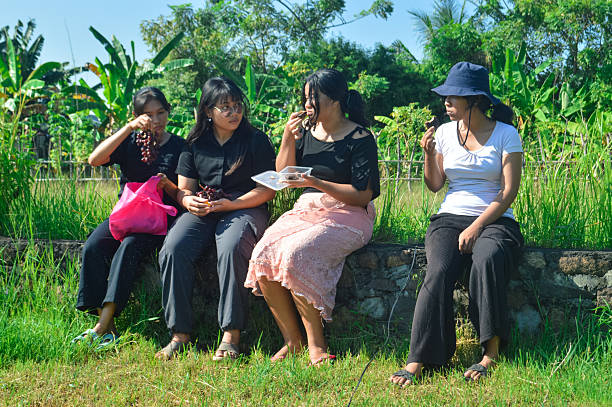 The girls sit closely together, exchanging stories and sharing fresh fruits and pastries in a quiet rural landscape.