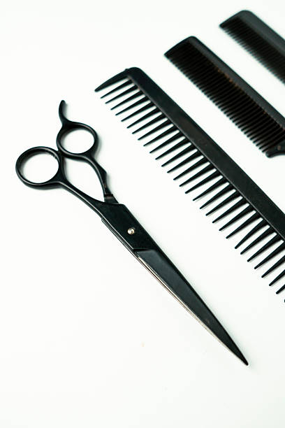 The image showcases a pair of black hairdressing shears and two black combs arranged on a clean white surface. The shears have a sleek, professional design, and the combs feature fine teeth. The tools are positioned in a visually appealing manner, emphasizing their sharp lines and elegant simplicity.  The overall impression is one of clean professionalism, suitable for a salon or barber setting.