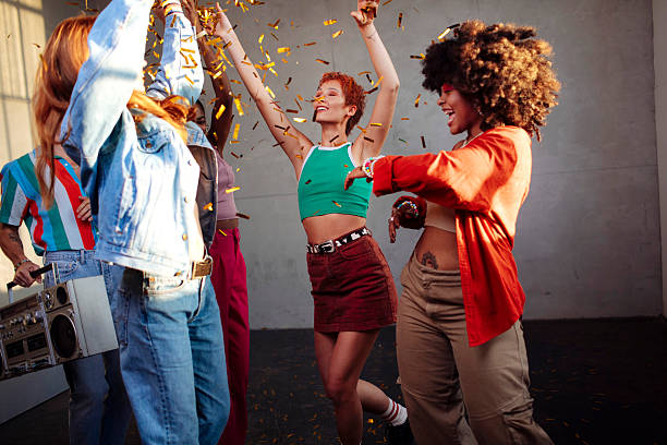 A diverse group of Gen Z friends celebrates joyfully and dancing in a photography studio with confetti, colorful outfits, and vibrant energy, showcasing multicultural diversity