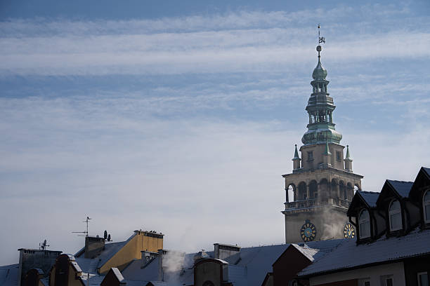 The historic clock tower of the Kłodzko Town Hall rises above snow-covered rooftops, with smoke curling from chimneys on a cold day. Picture taken on a holiday trip to Kłodzko, Poland with my Sony a7III.