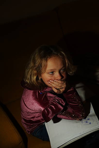 A child with a thoughtful expression rests their chin on their hand while holding a pencil. A notebook with drawings is visible, suggesting a moment of creative contemplation.